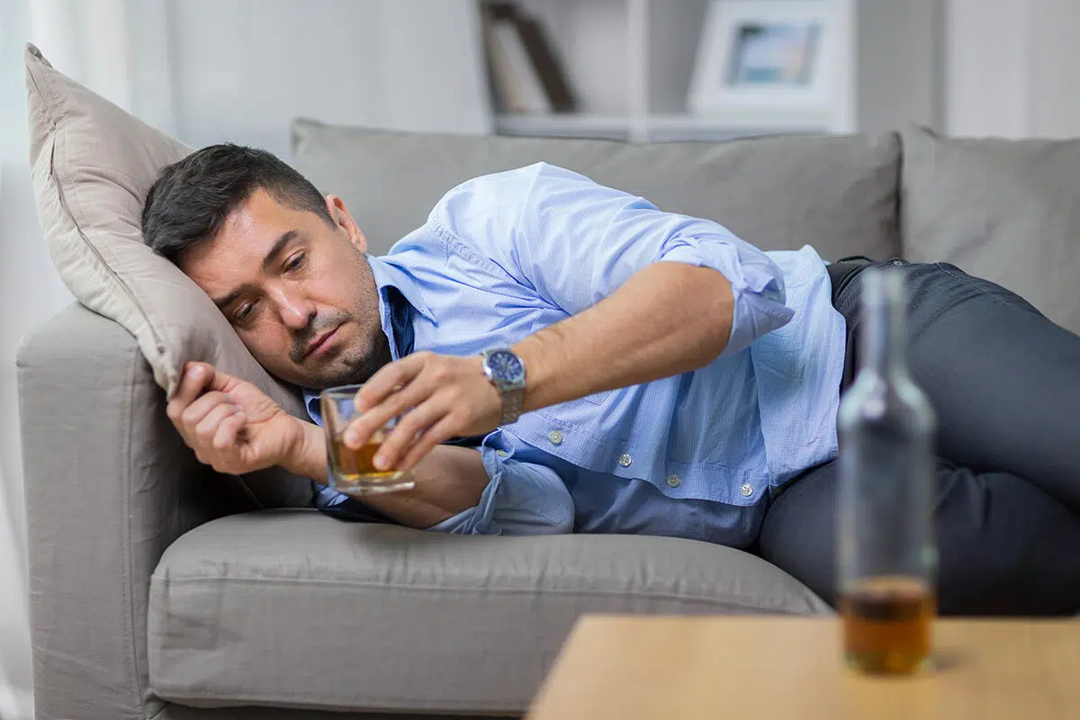 man laying on couch drinking alcohol because of Alcohol Dependence