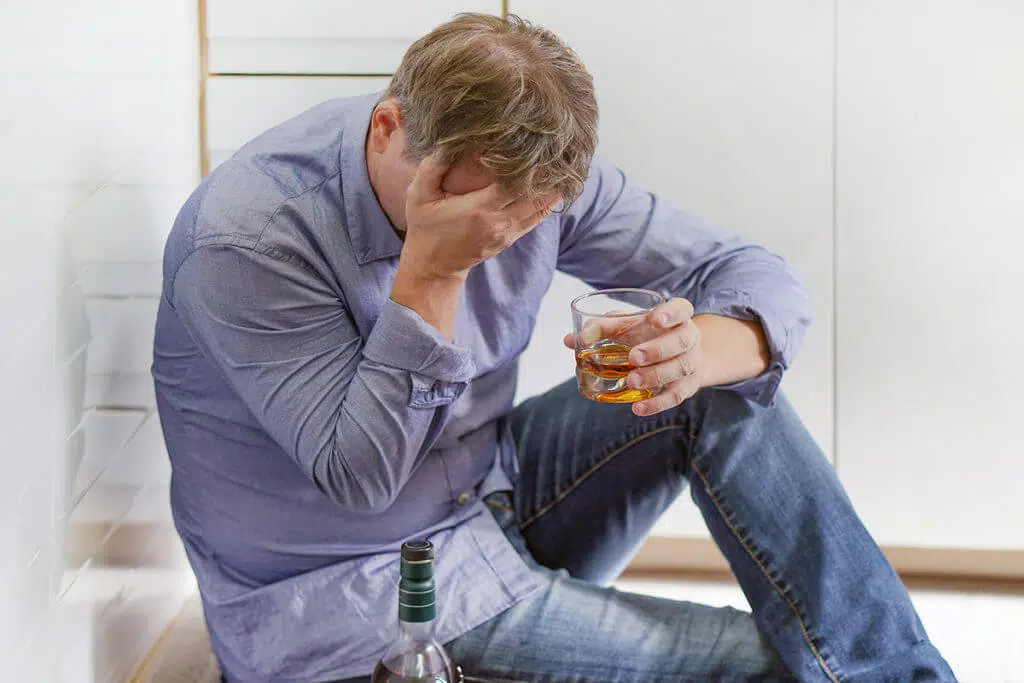 man on the floor with glass of alcohol wondering am i an alcoholic