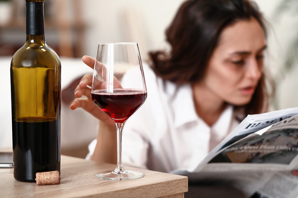 disheveled woman reaching for glass of wine showing Signs of Alcoholism