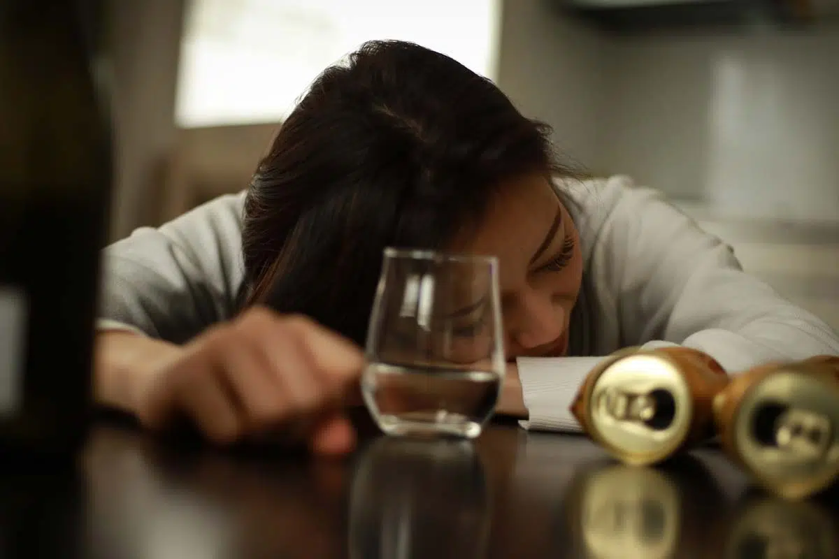 woman passed out next to alcohol on table showing the signs of alcohol overdose