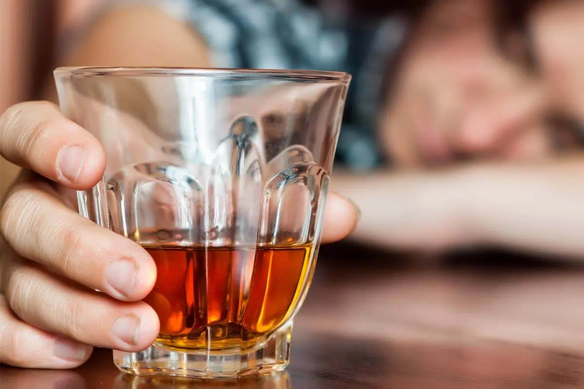 person passed out on table with glass of alcohol going through Stages of Addiction