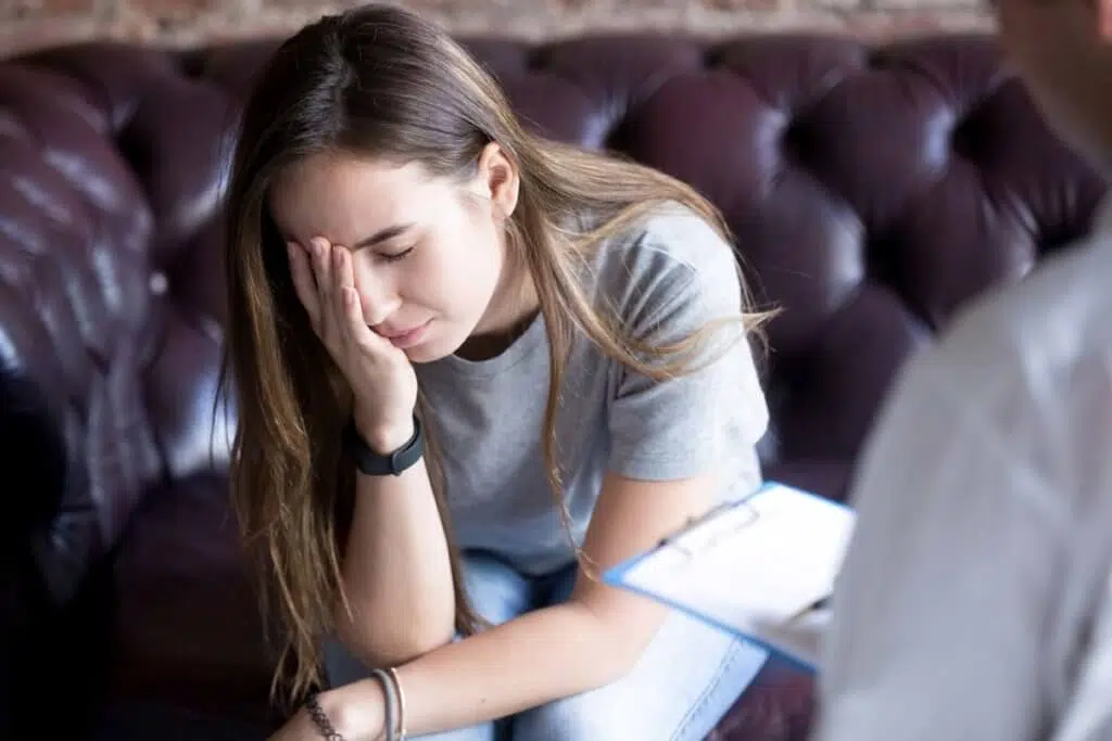 young woman covering her face in therapy dealing with Types of Trauma