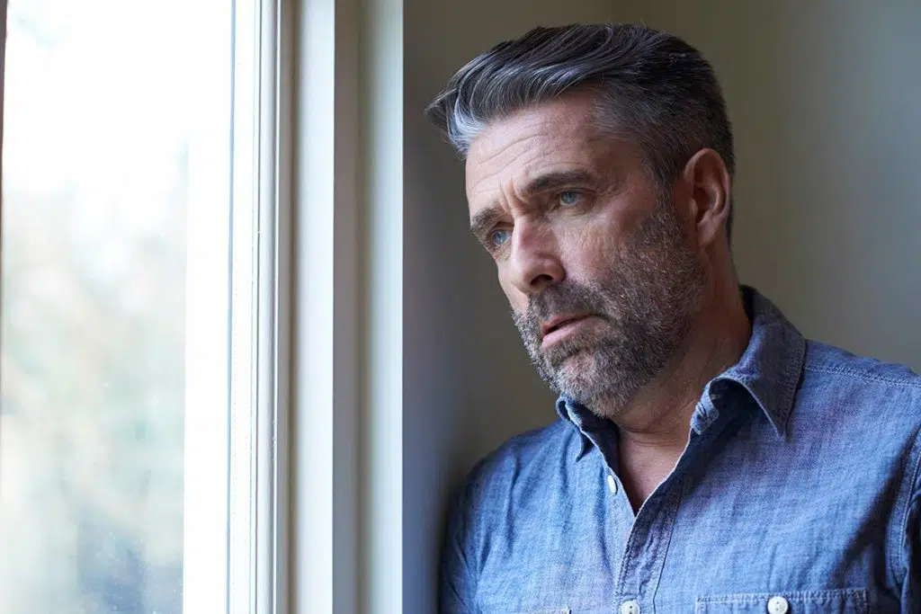 man looking forlorn out window due to addiction